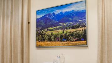 Une chambre d’hôtel avec une table, deux chaises, un climatiseur et un grand tableau représentant un paysage accroché au mur.