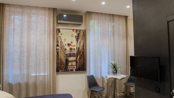 A hotel room with a bed, a desk with a chair, a TV, and a window with curtains.