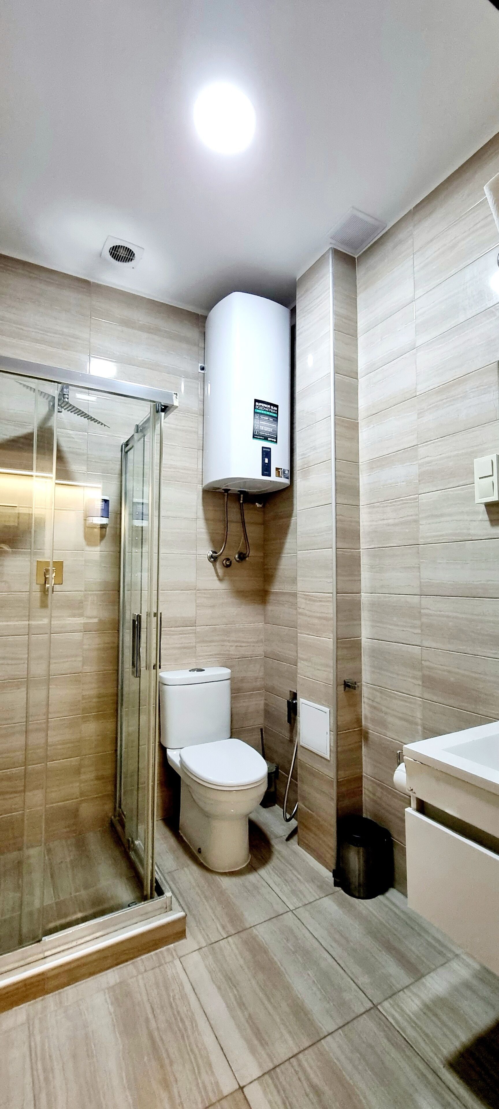 A modern bathroom with a glass-enclosed shower, a toilet, and a built-in sink.