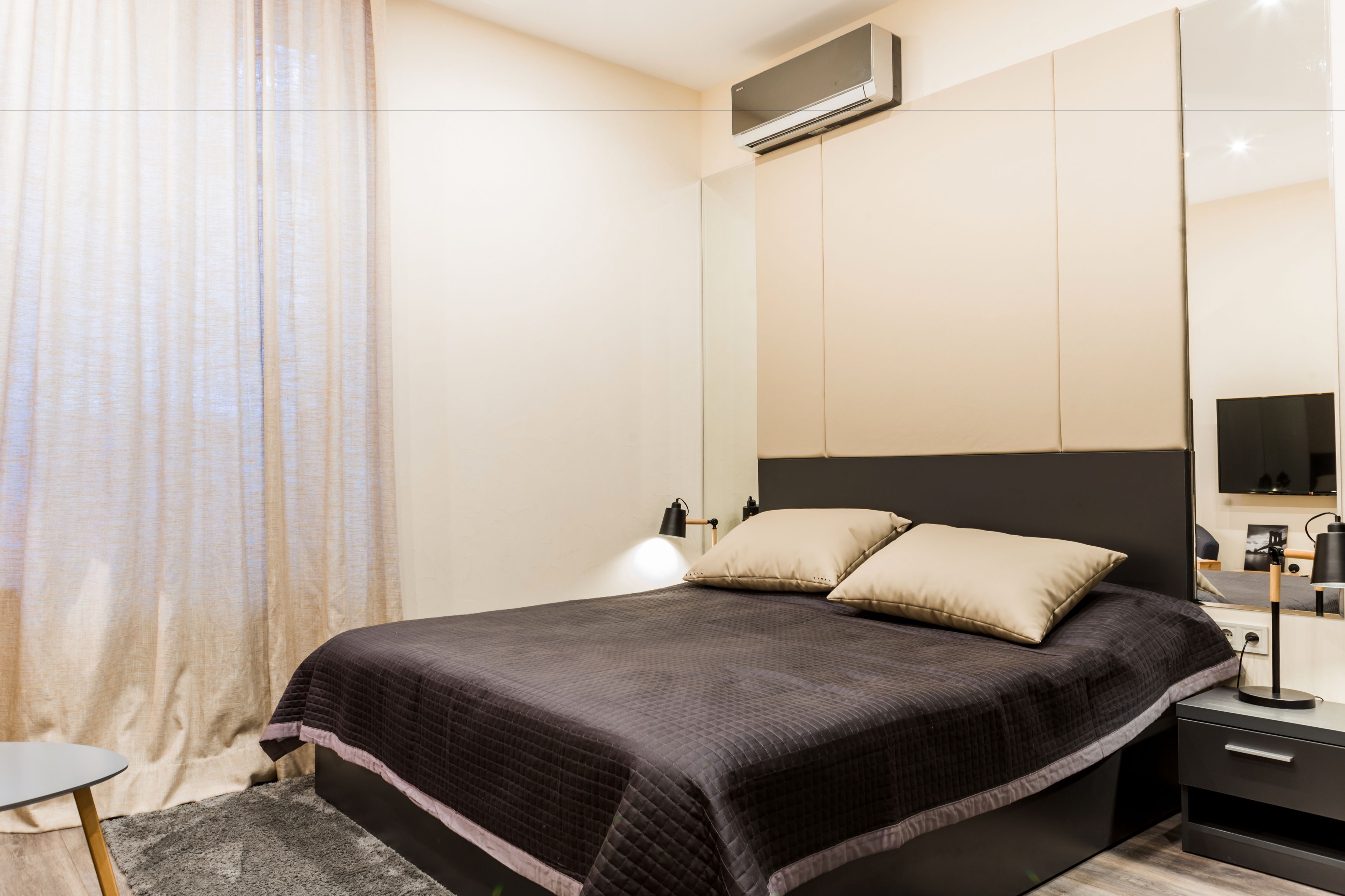 Ein modernes Schlafzimmer mit einem großen Bett, Nachttischen, einem Fernseher und einem Fenster mit Vorhängen.