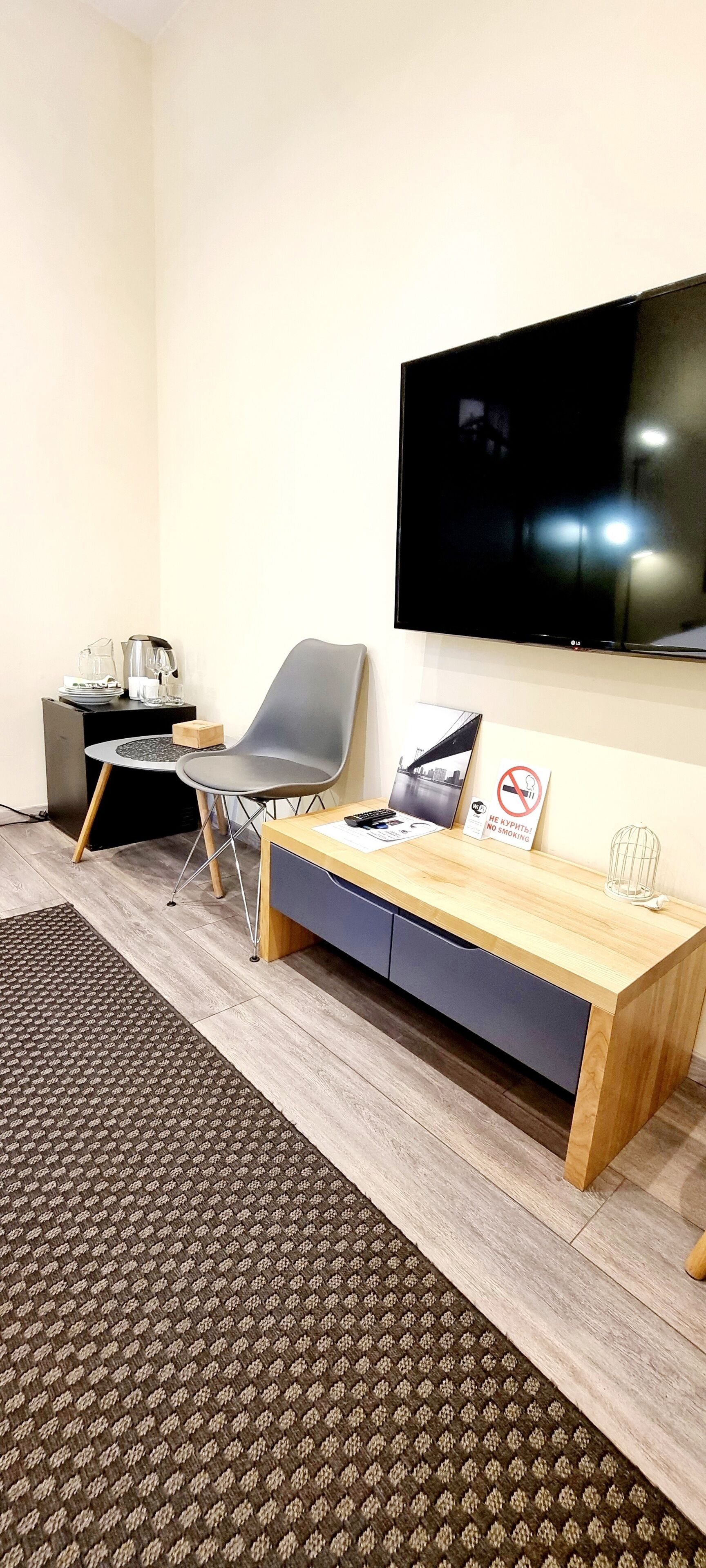 Una habitación moderna con un escritorio de madera, un televisor de pantalla plana, una silla, una mesita con una cafetera y un cartel de 'No Smoking'.