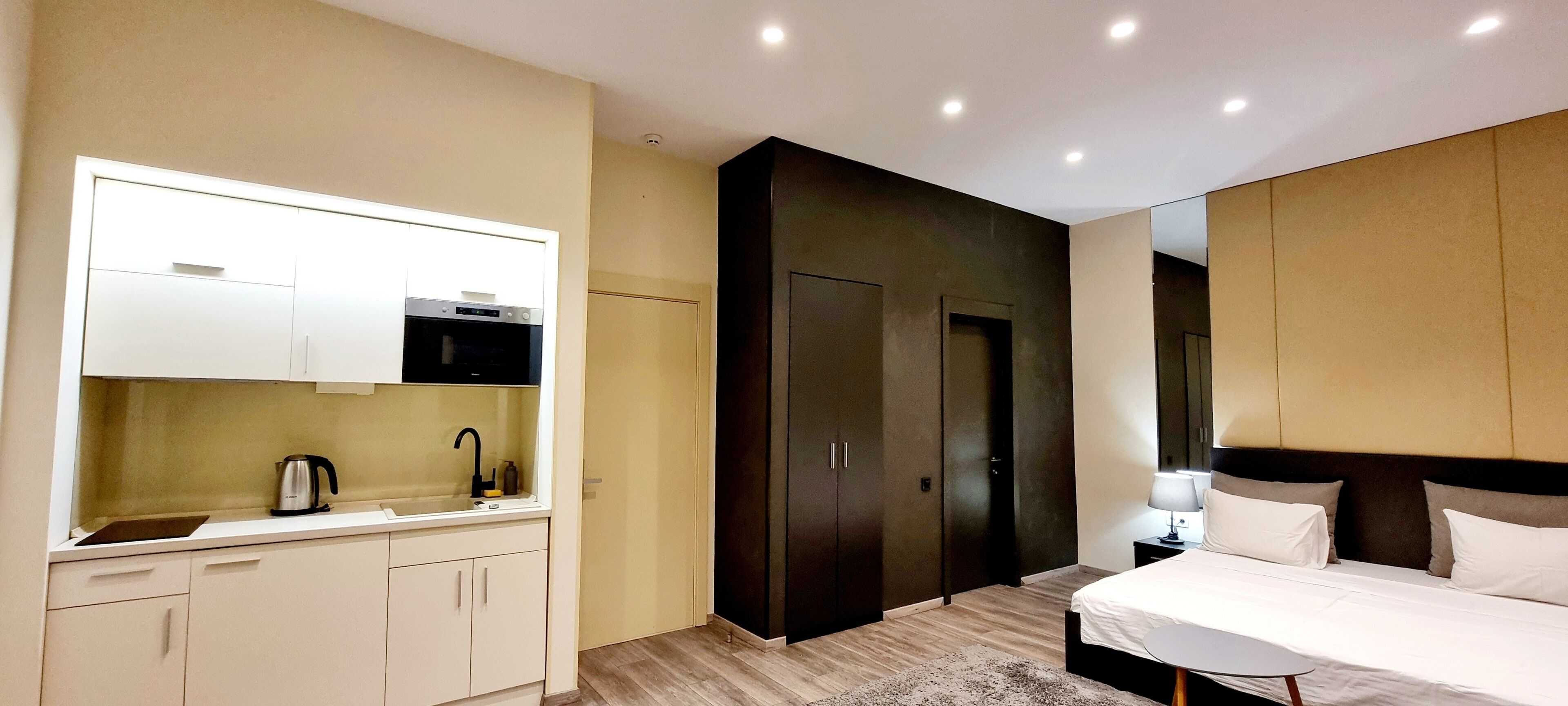 Una habitación de hotel moderna con kitchenette, una cama grande y un armario oscuro.