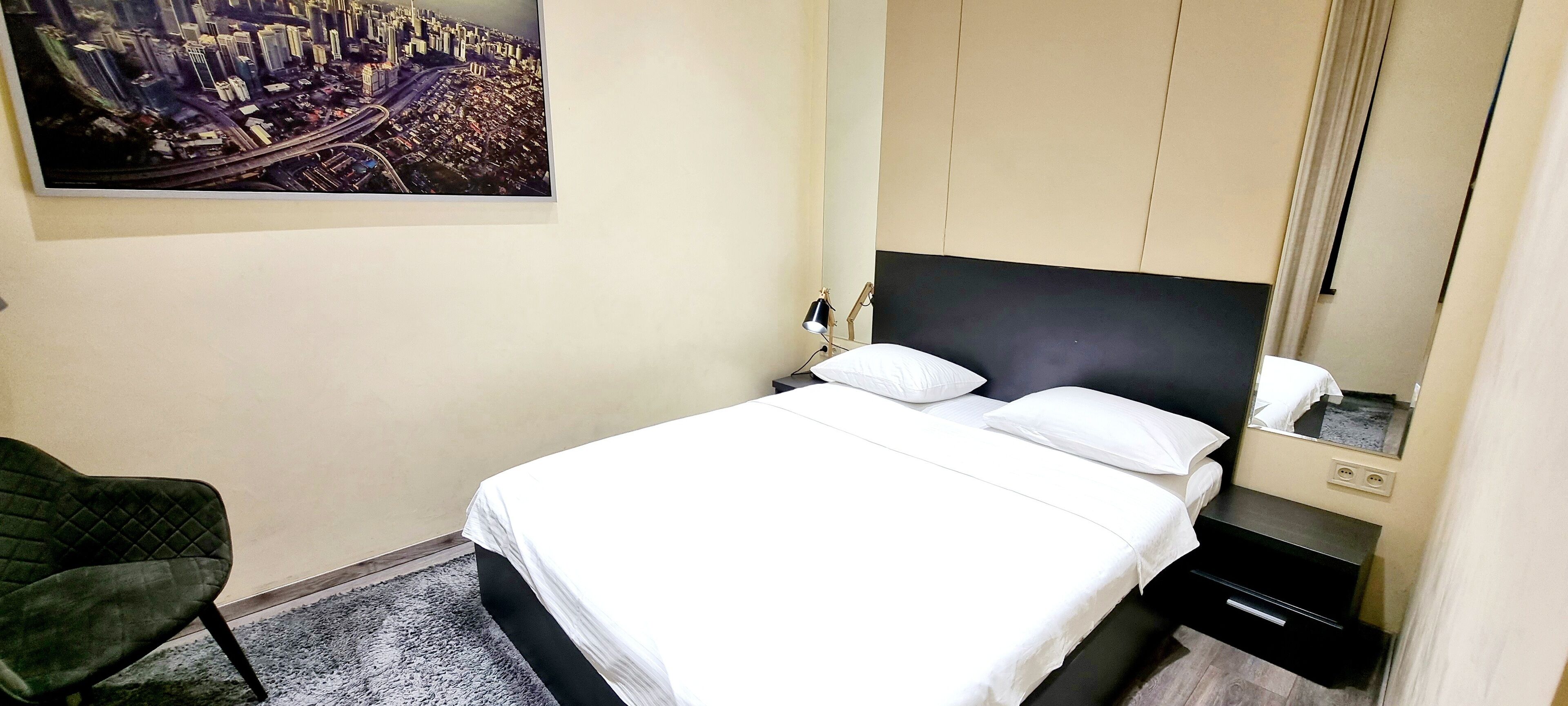 Une chambre d’hôtel comprenant un lit, une table de chevet, une chaise, un grand tableau représentant un paysage urbain et un miroir.