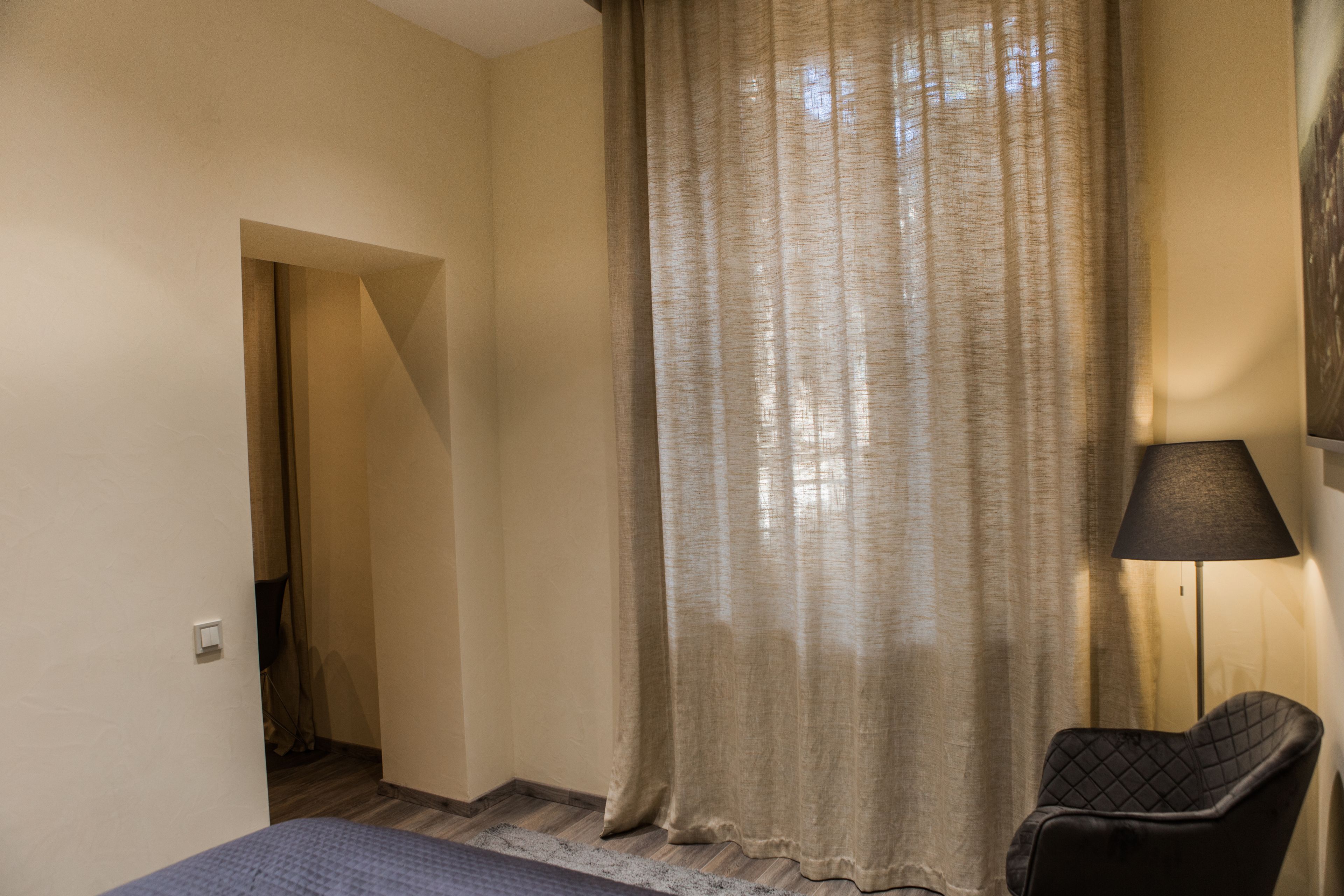 Un dormitorio con cama, una silla, una lámpara y un ventanal con cortinas.