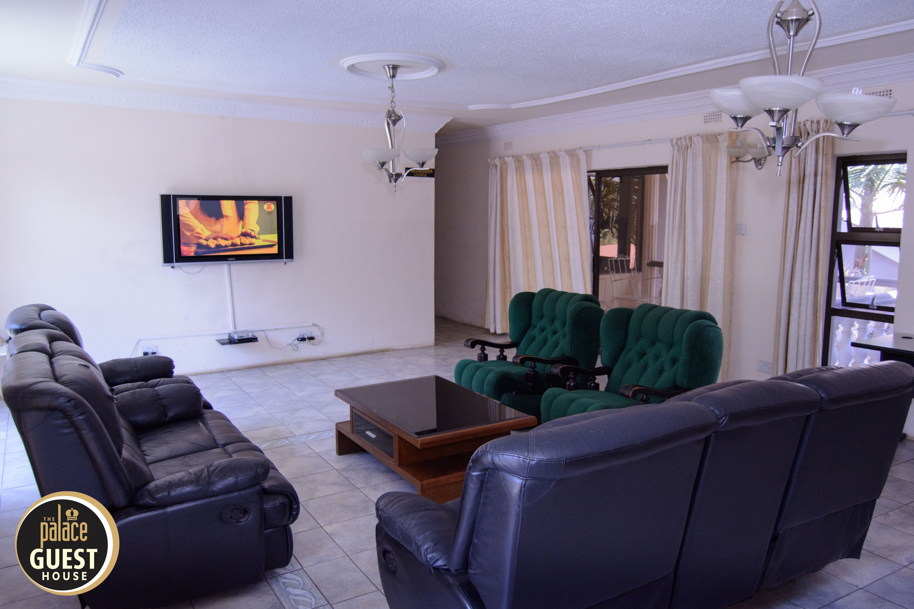 A modern living room with a black leather sofa, a green tufted chair, and a flat-screen TV mounted on the wall.
