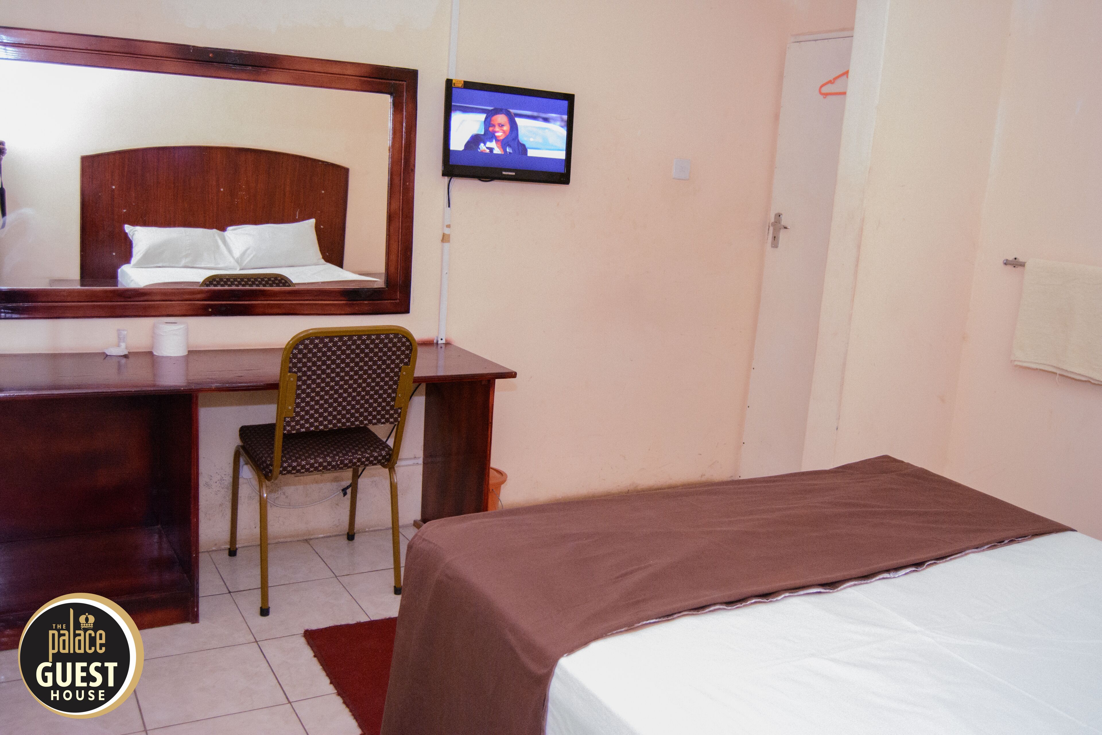 A hotel room with a bed, a desk with a chair, a television, and a mirror.