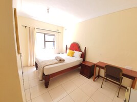 Una habitación de hotel con cama, mesita de noche, silla y ventana con cortinas.
