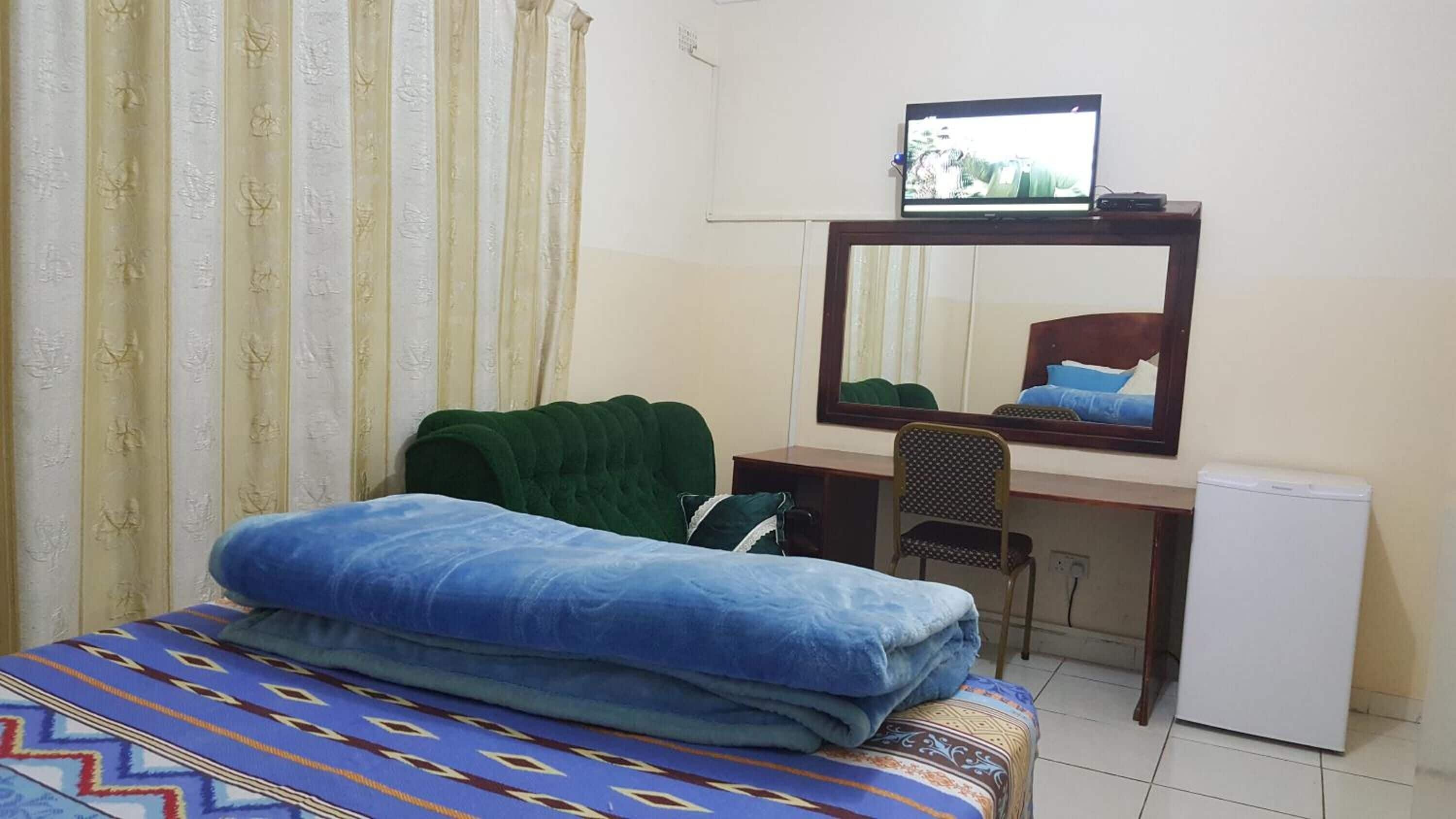 Un dormitorio con cama, escritorio, silla, televisor y un refrigerador pequeño.