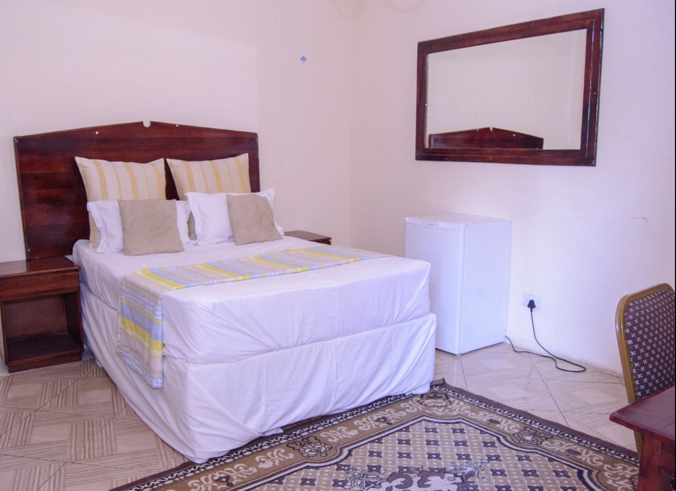 A bedroom with a bed, bedside tables, a dresser, a mirror, a radiator, and a patterned rug.