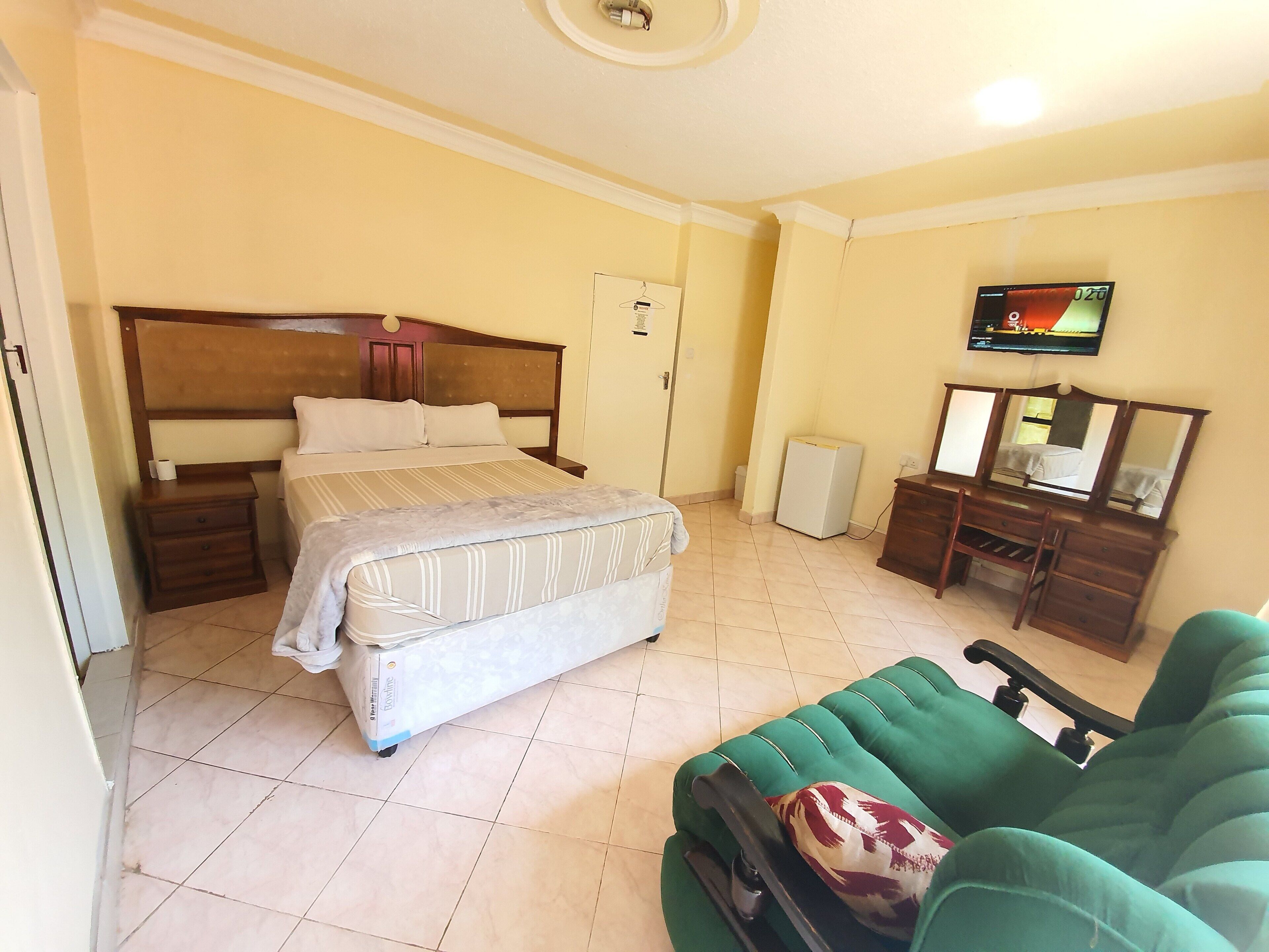 A hotel room with a bed, a green sofa, a dresser, a mirror, and a television.