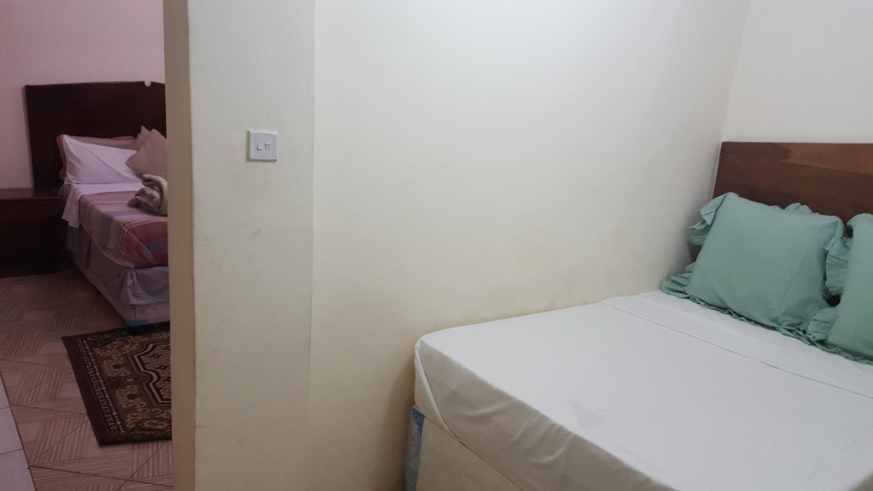 A bedroom with a bed, a nightstand, a lamp, and a wall socket.