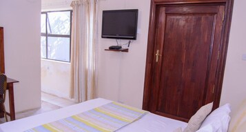 Un dormitorio con cama, televisor montado en la pared, puerta de madera y ventana con cortinas.