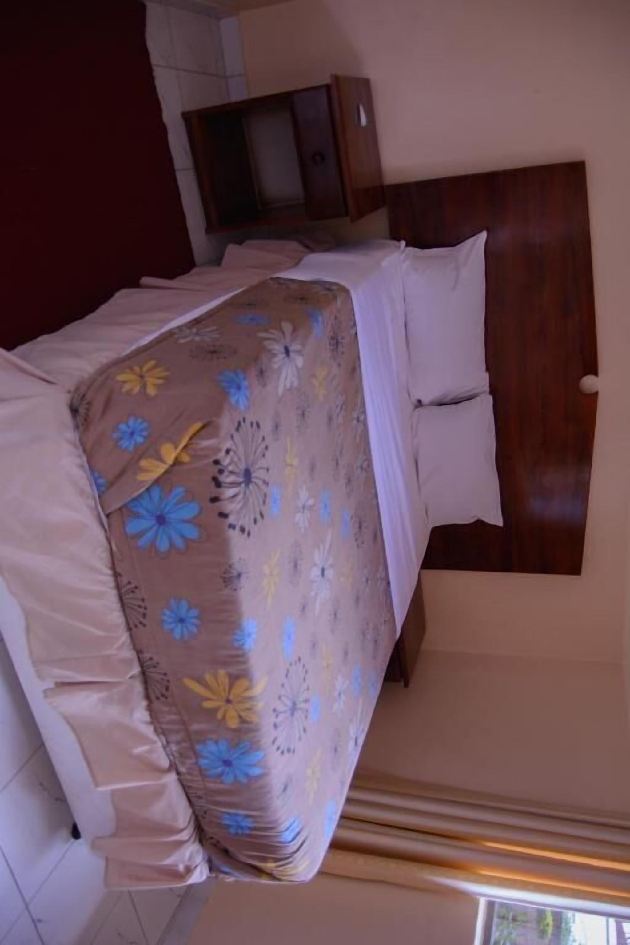 Un lit avec une couvre-lit à motifs floraux, une tête de lit en bois et des oreillers blancs.