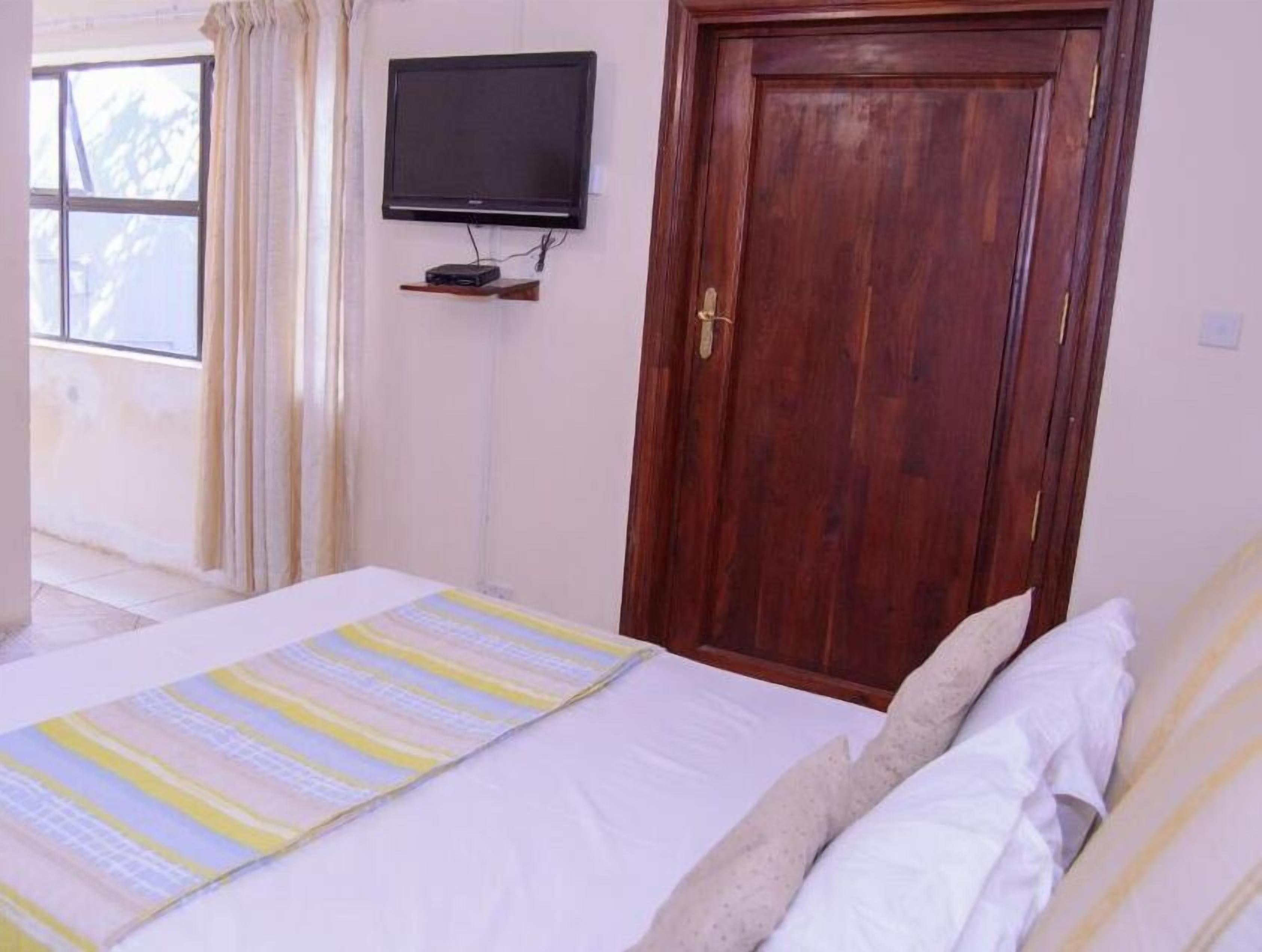 Un dormitorio con una cama, televisión montada en la pared y una puerta de madera.