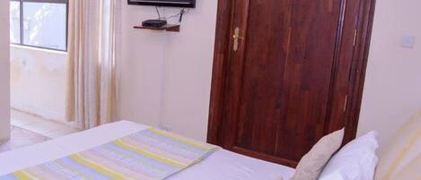 Un dormitorio con una cama, televisión montada en la pared y una puerta de madera.