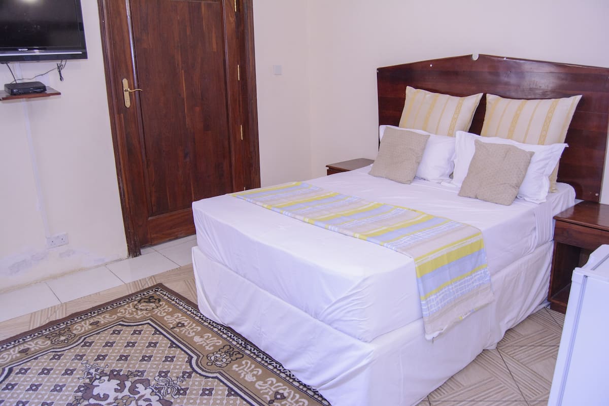 Cama bem arrumada com coberta listrada, cabeceira de madeira e várias almofadas.