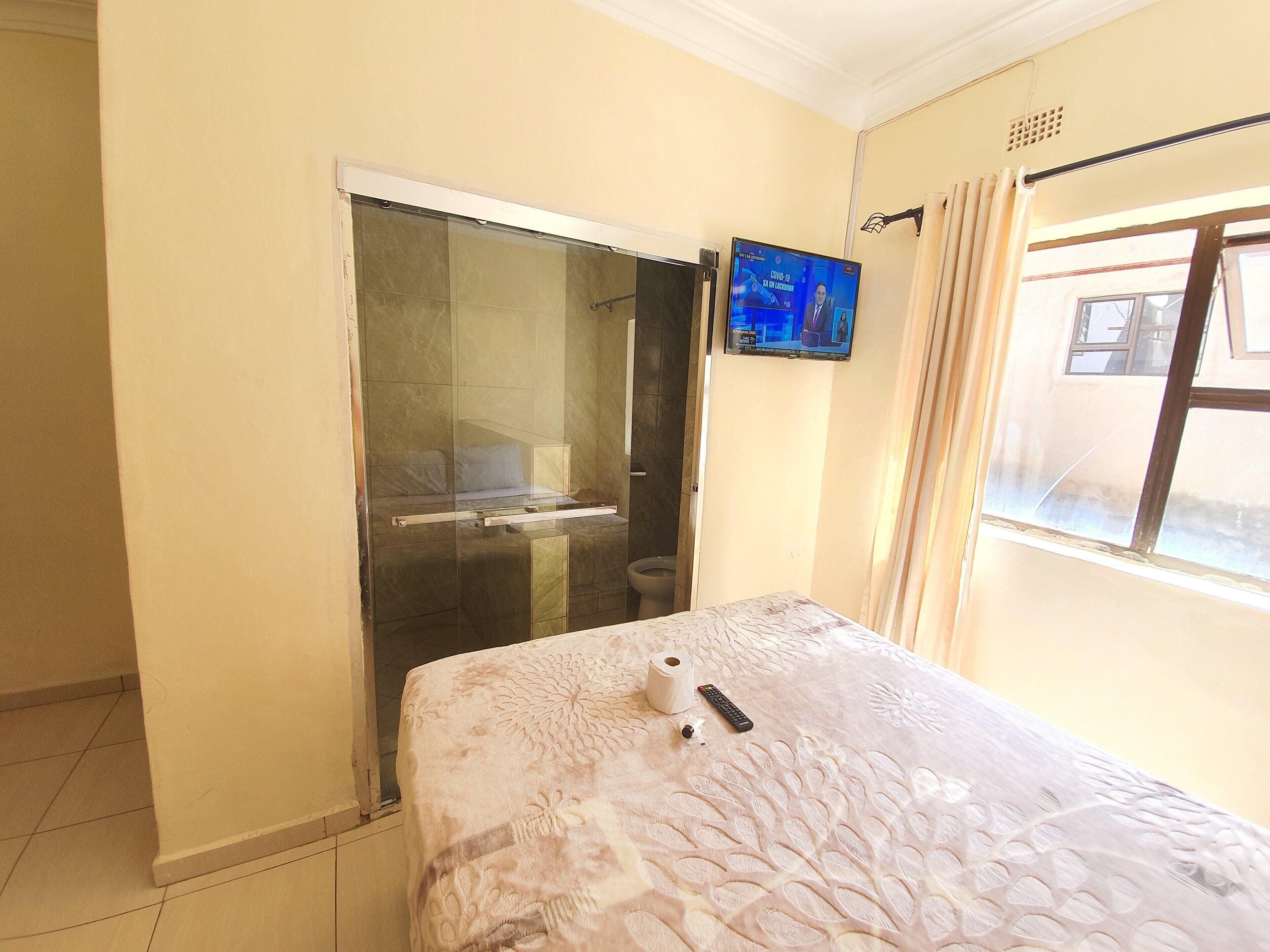 A hotel room with a bed, a television, a bathroom, and a window.