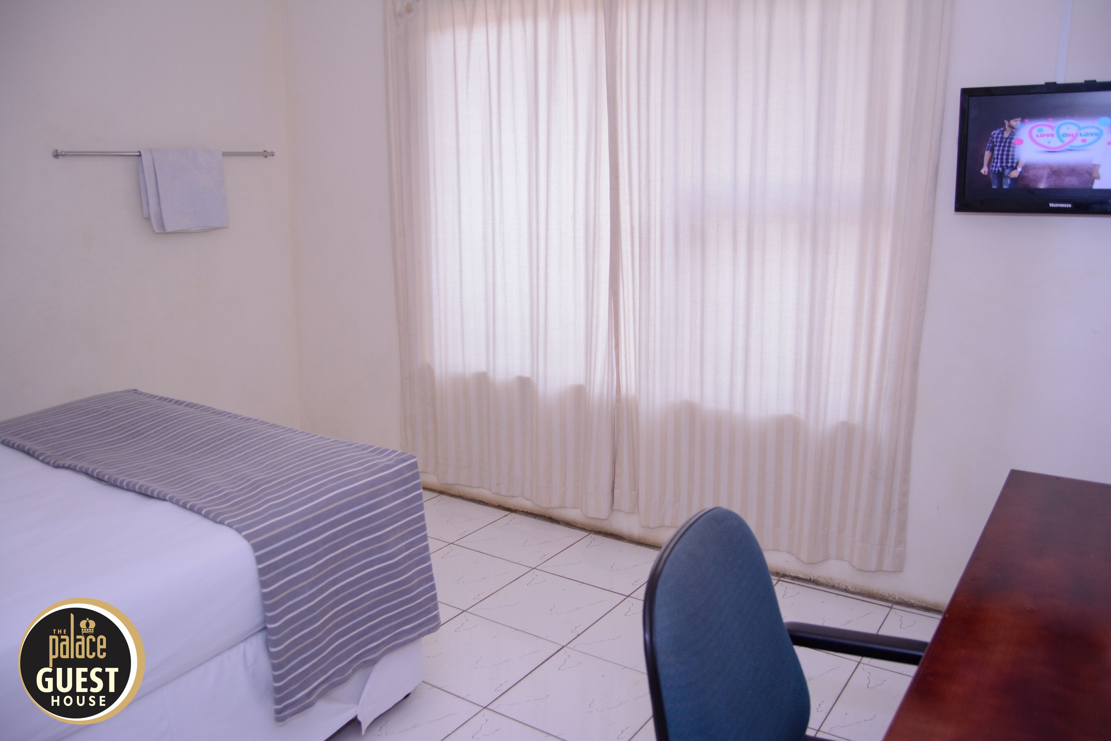A hotel room with a bed, a desk, a chair, a TV, and a window with curtains.