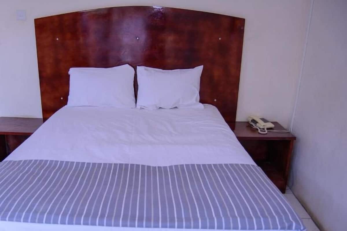 Cama bem arrumada com roupa de cama branca e manta listrada, cabeceira de madeira e mesa de cabeceira com telefone.