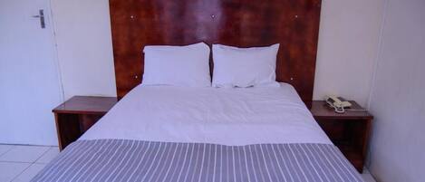 A neatly made bed with a striped bedspread, two white pillows, and a wooden headboard. There are two bedside tables, one with a telephone on it.