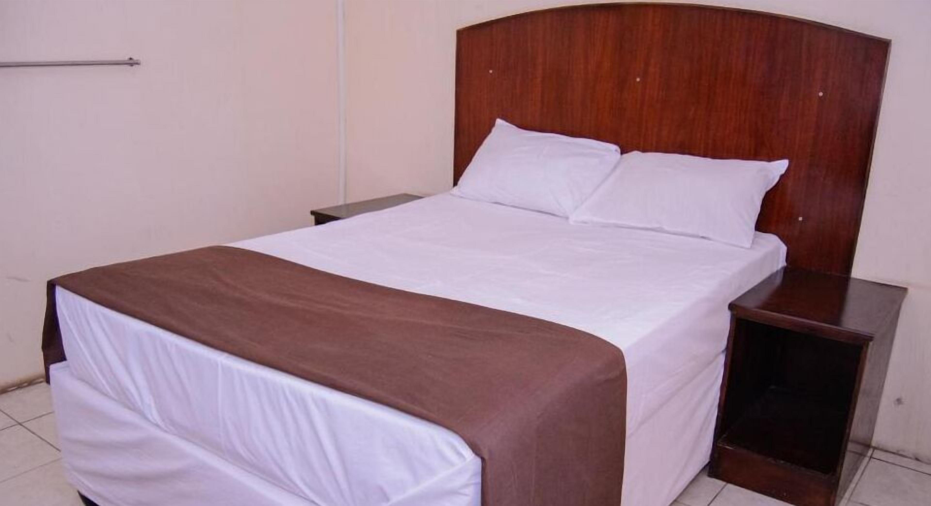 A single bed with a wooden headboard, white bedding, and a brown accent.