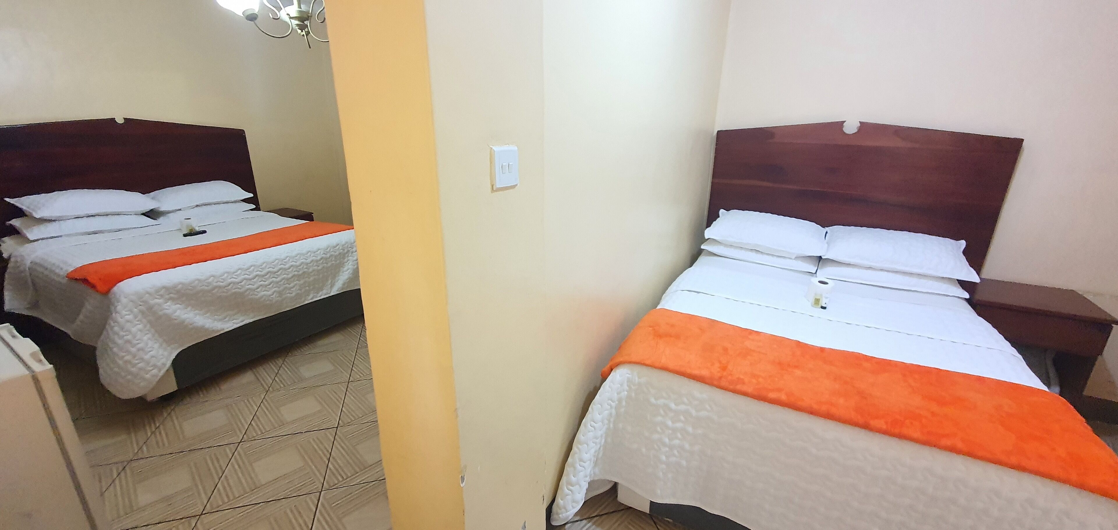 Dos camas con cabeceros de madera, ropa de cama blanca y mantas color naranja.