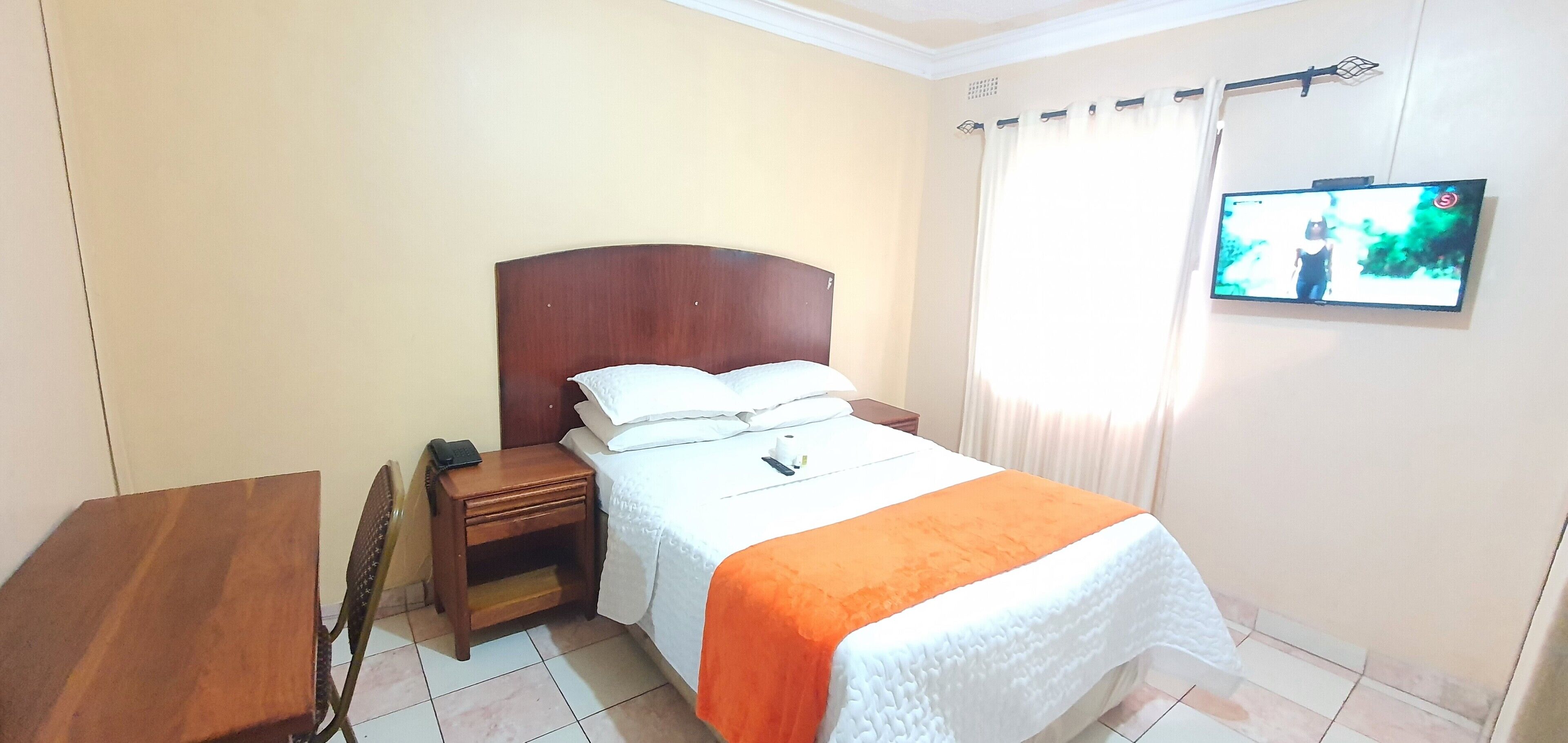 Un dormitorio con una cama, una mesita de noche, una mesa de madera y un televisor en la pared.
