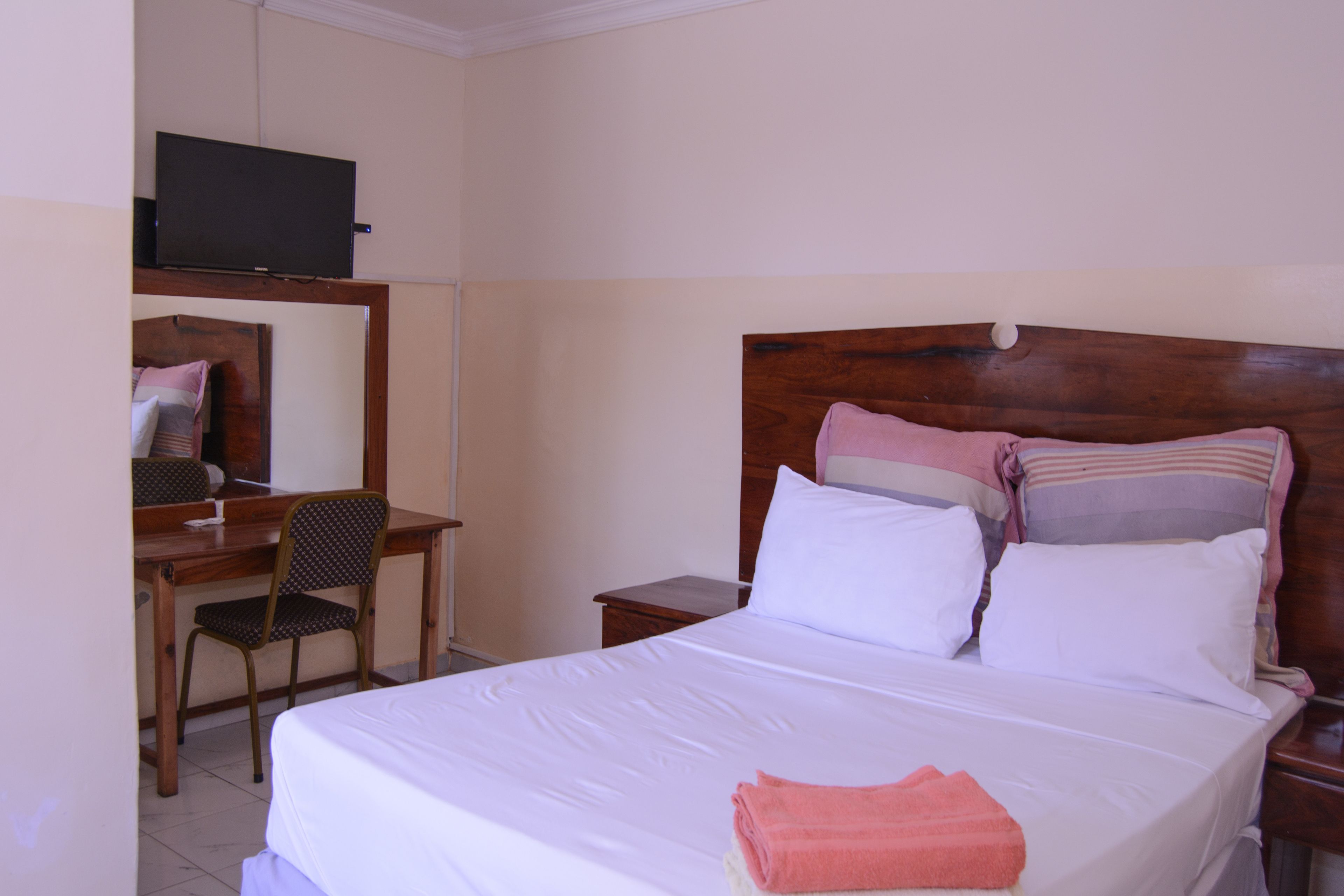 A hotel room with a bed, a desk, a chair, a television, and a mirror.