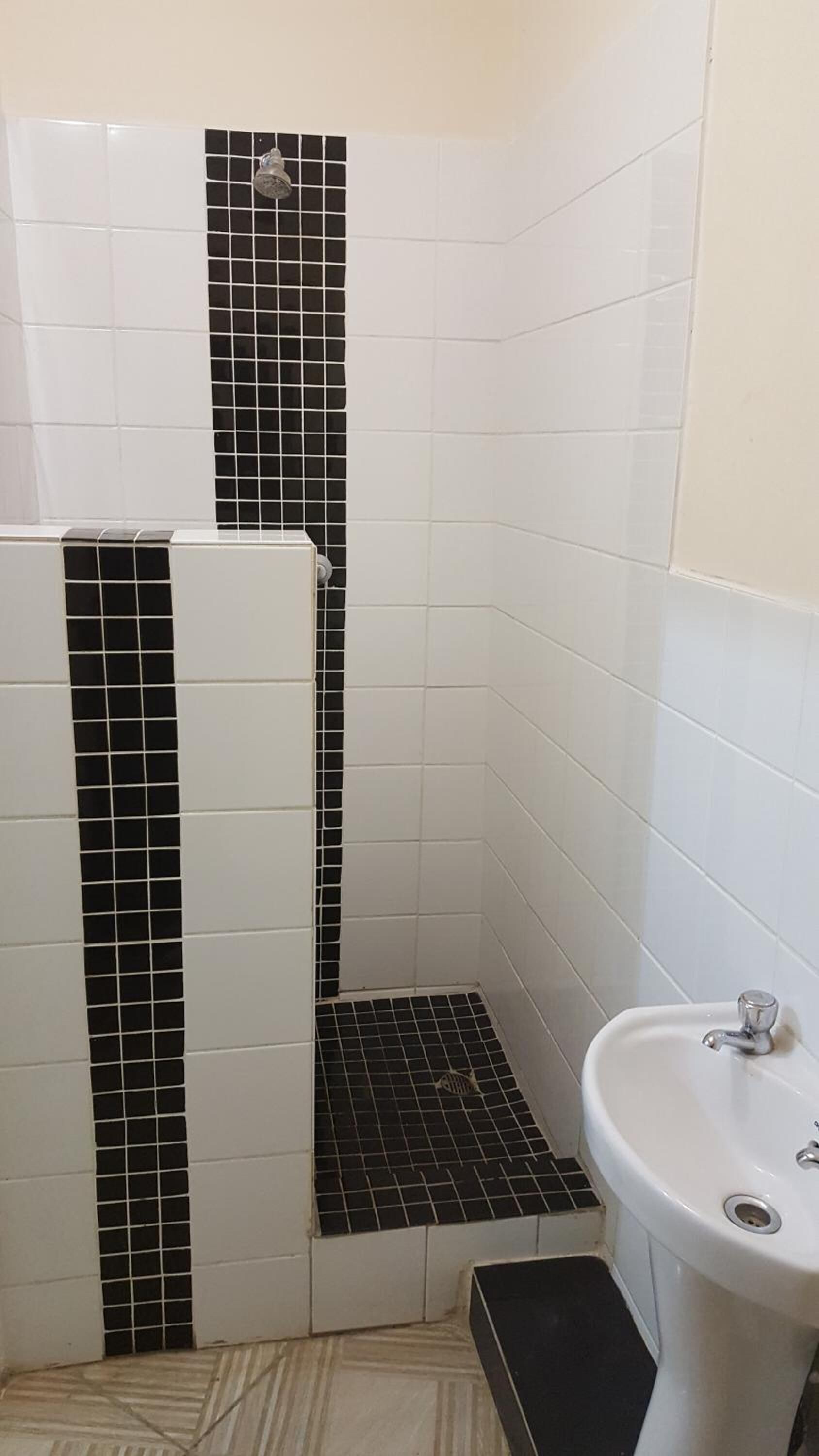 A bathroom with white tiles, a black-tiled shower area, and a white sink.