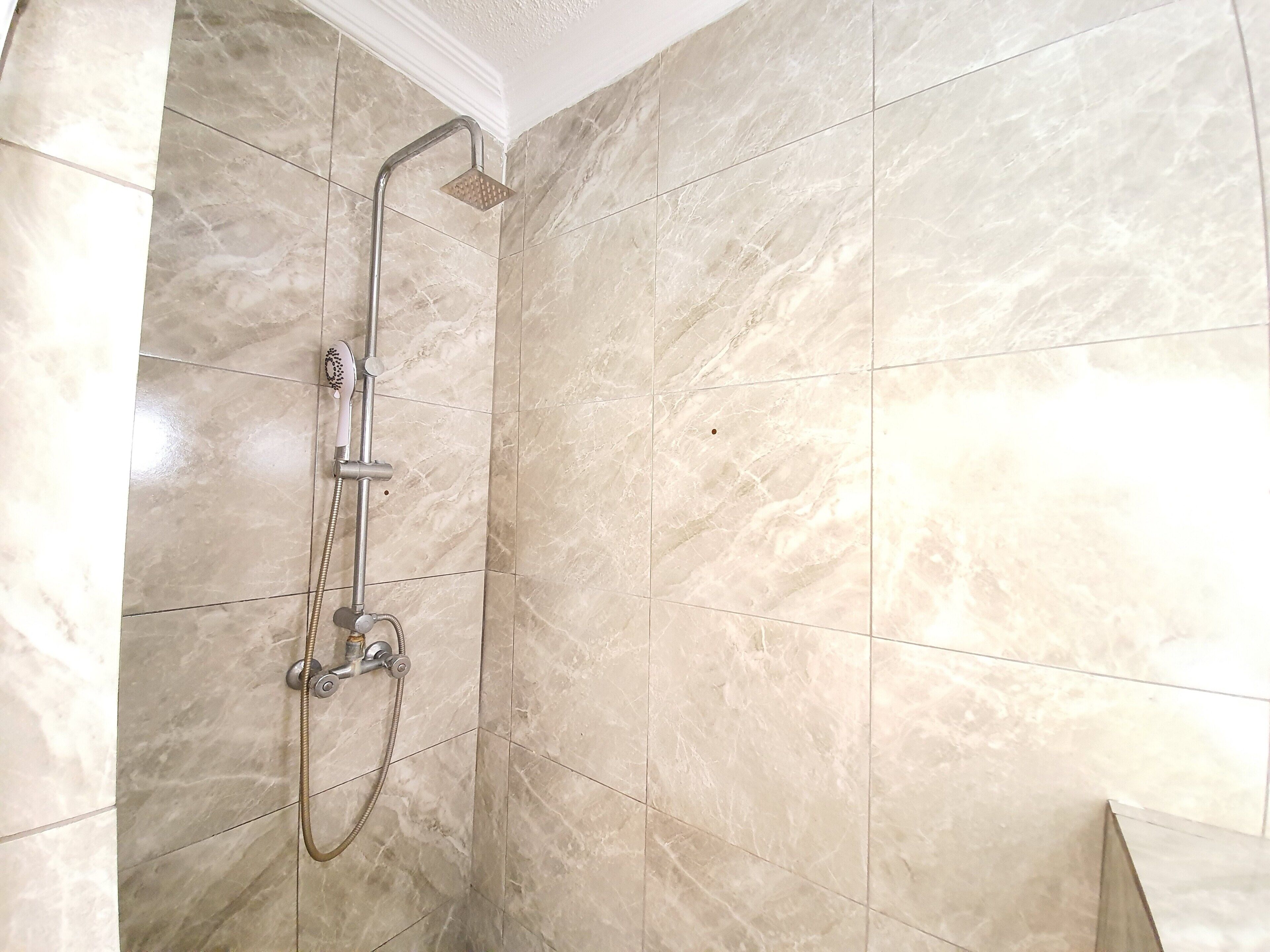 Un baño con ducha, paredes de azulejos y un lavamanos en esquina.