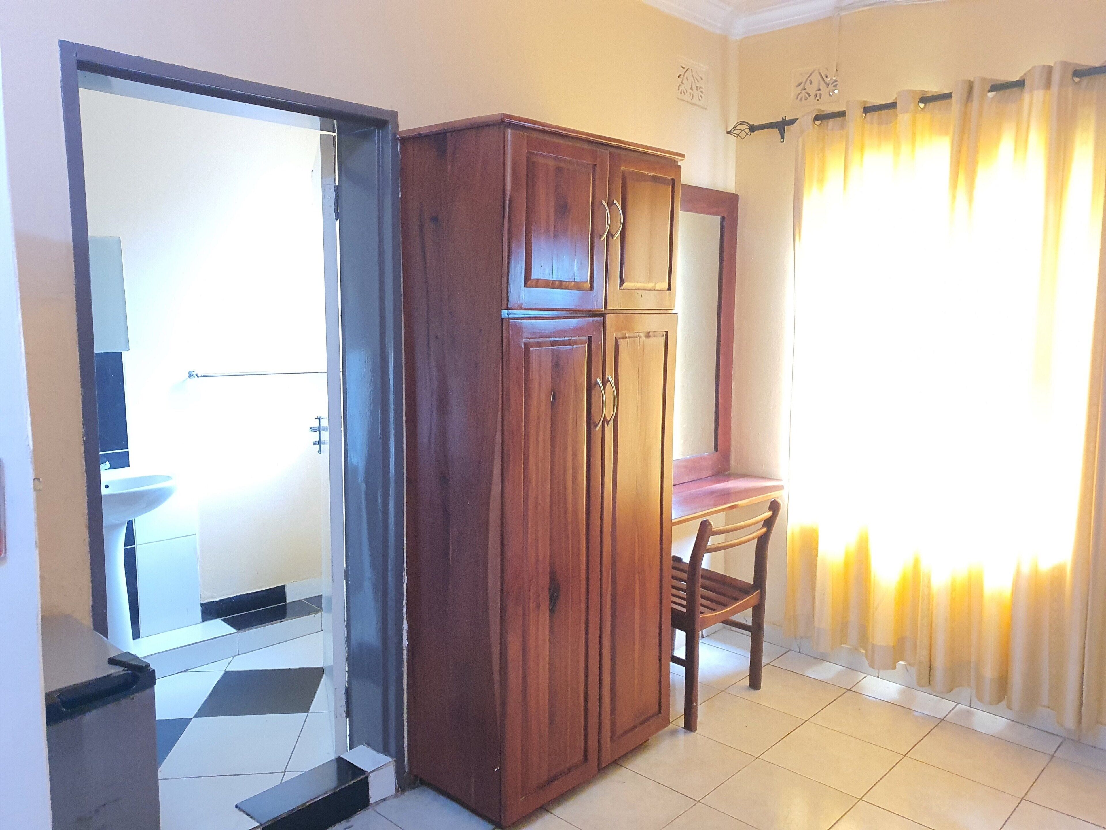 Una habitación con un armario de madera, una silla, suelo de baldosas y una ventana con cortinas.