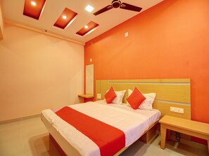 A hotel room with a bed, a bedside table, a mirror, and a ceiling fan. - Capital O 13489 Garuda Comforts (Mangaluru)