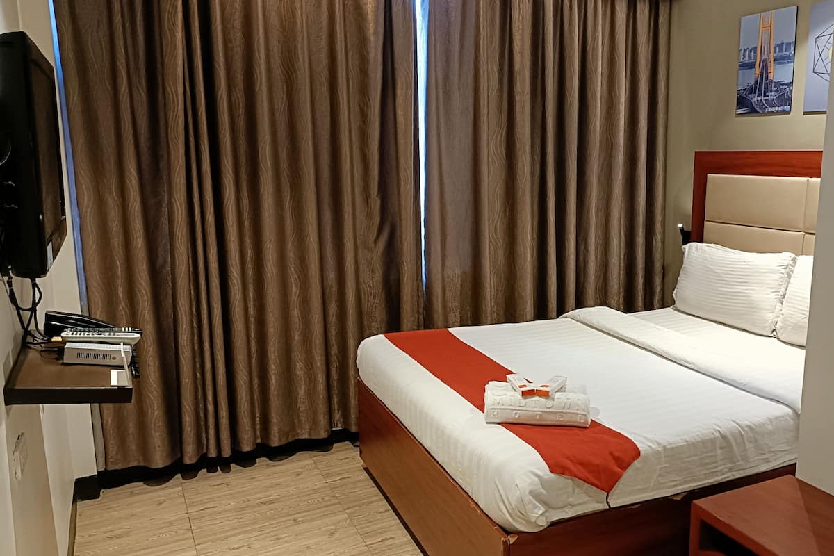 A hotel room with a bed, a nightstand, a TV, and curtains.