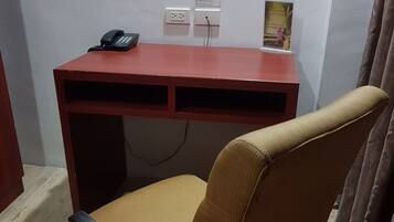 A red desk with a black telephone, two electrical outlets, and a framed picture on the wall.