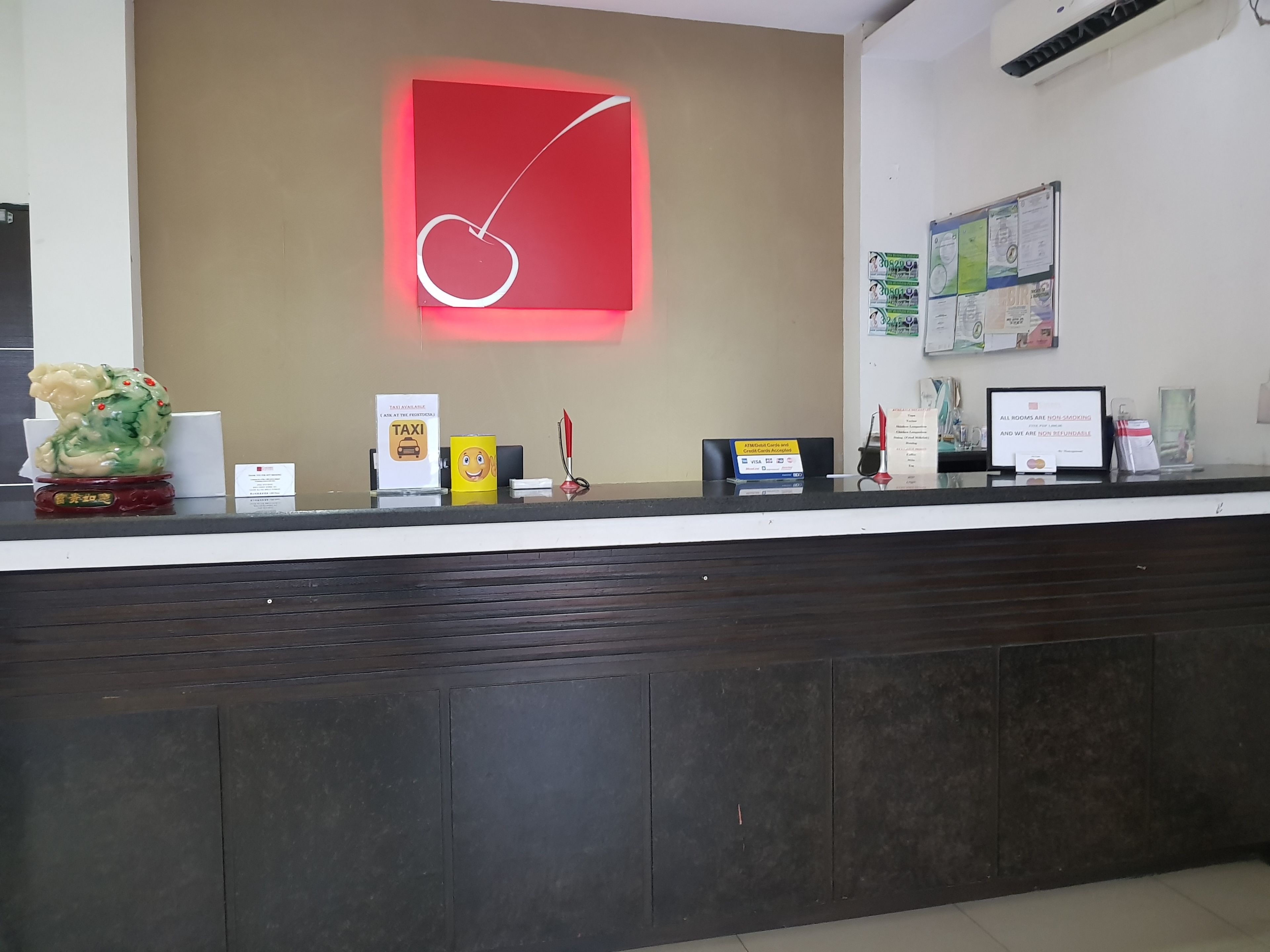 A hotel reception desk with a red neon sign, a decorative statue, a taxi sign, and various informational signs.
