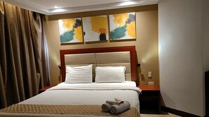 A hotel room with a large bed, two pillows, a wooden headboard, and three abstract paintings on the wall. - Cherry Midtown Hotel (Olongapo)