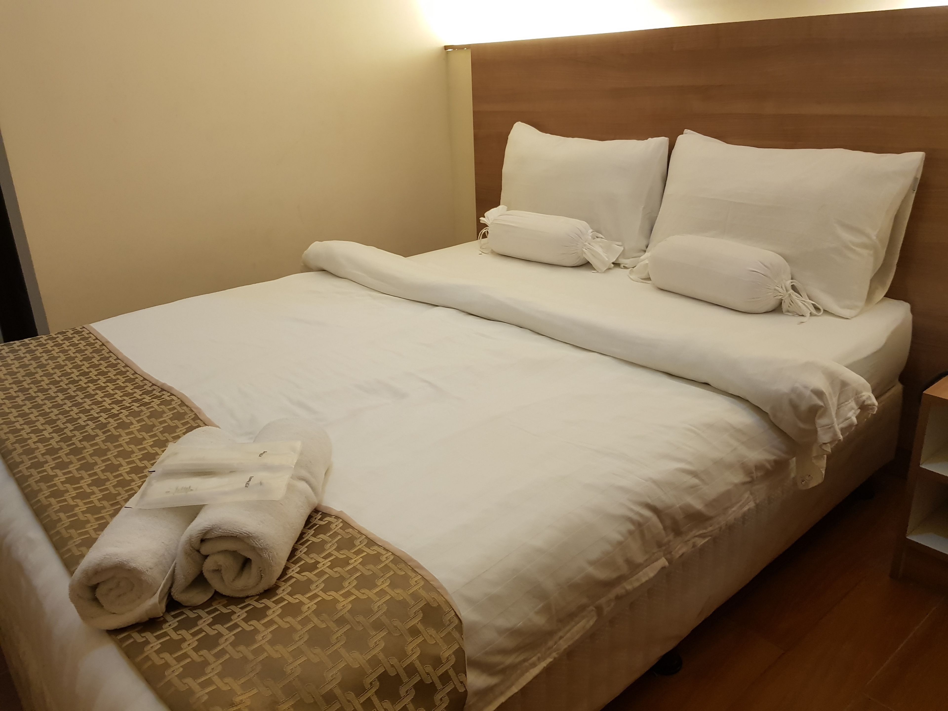 Una cama bien hecha con sábanas blancas, un edredón estampado y toallas dobladas a un lado.