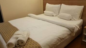 Una cama bien hecha con sábanas blancas, un edredón estampado y toallas dobladas a un lado.