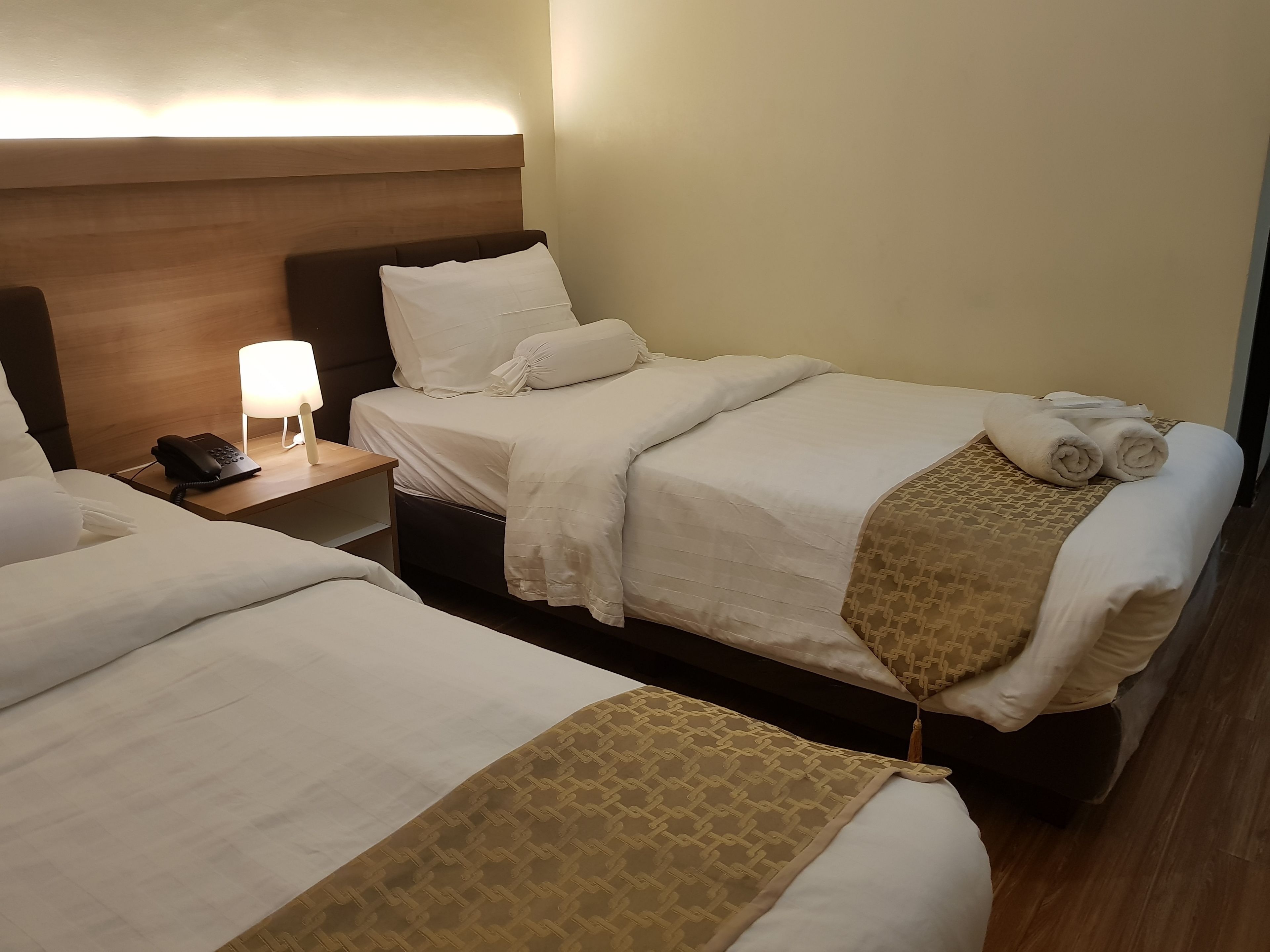 A hotel room with two beds, a bedside table with a lamp, and a phone.