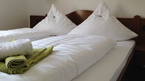 A neatly made bed with white linens and two pillows, a green towel, and a wooden headboard. - Hotel Rose (Ebersbach an der Fils)