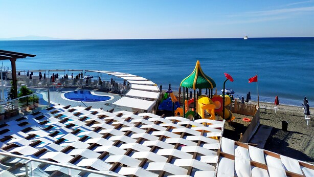 Un resort frente a la playa con piscina, sillas de descanso y una zona de juegos.