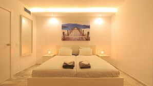 Habitación de hotel con una cama grande, dos mesitas de noche, un cuadro sobre la cama y vistas a un muelle que da a un cuerpo de agua.