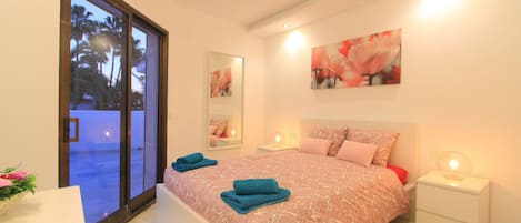 A bedroom with a bed, two bedside tables, a nightstand, a large window, and a door.