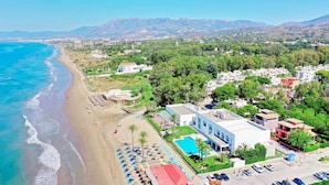 Vista aérea de una zona costera con playa, piscina y una combinación de edificios residenciales y comerciales.