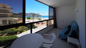 A balcony with a view of the beach, a white table, and a blue chair.