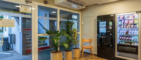 A reception area with a vending machine, potted plants, and a wooden chair.