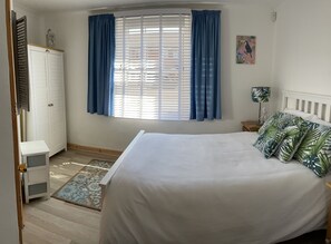 A bedroom with a bed, a wardrobe, a window with curtains, a nightstand, and a lamp.