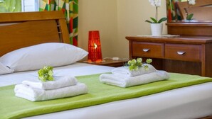 A neatly made bed with white towels and a green blanket, a wooden nightstand with a red lamp, a wooden dresser, and a potted orchid. - Ayia Napa Tropical Beach Villa (Ayia Napa)