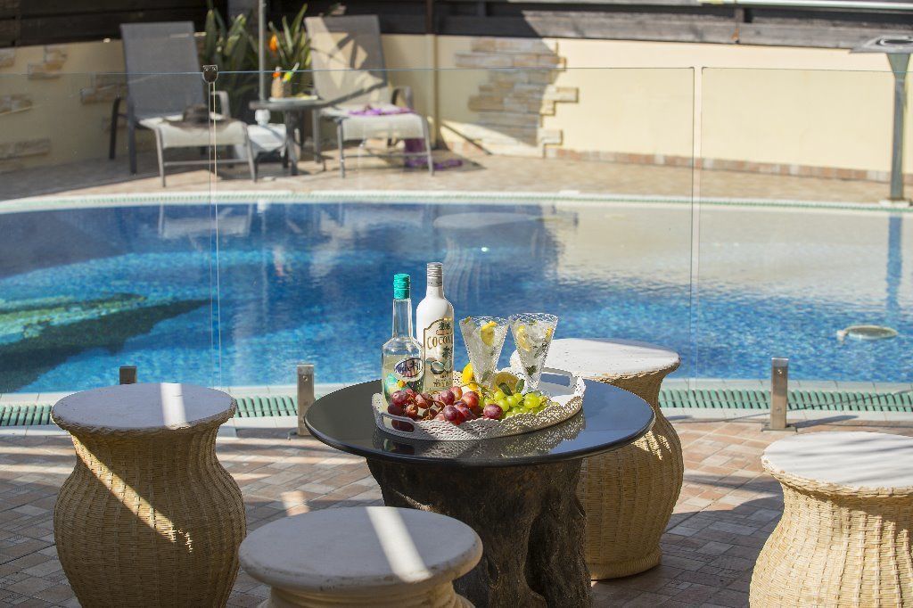 Un espace aménagé au bord de la piscine, avec des meubles en osier et une table sur laquelle sont disposées des bouteilles et des fruits.