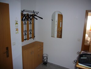 Une pièce comprenant une armoire en bois, un porte-manteau avec des cintres, un miroir et un téléphone posé sur un support.